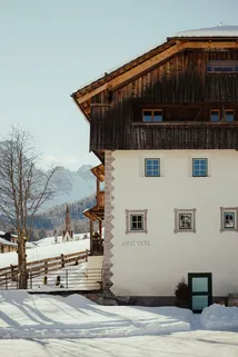 Ostí Vedl with snow-covered roof and walls set against a backdrop of snowy mountains.